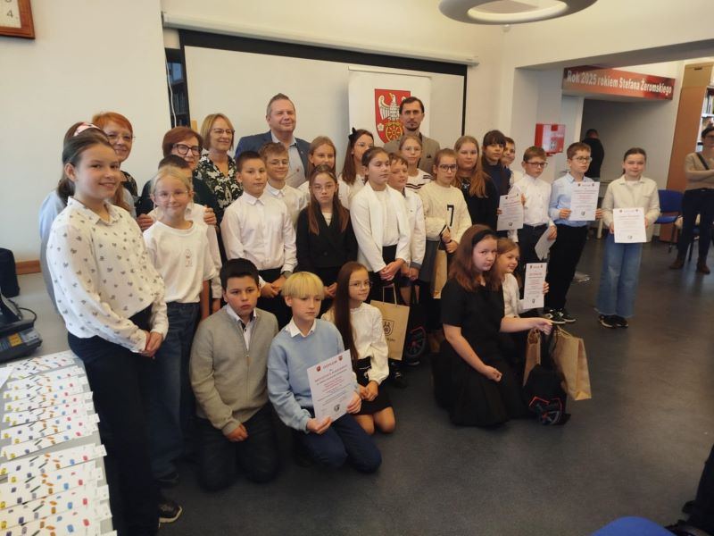 Na zdjęciu widać grupę dzieci i dorosłych pozujących do wspólnego zdjęcia po wręczeniu dyplomów i nagród podczas finału powiatowego konkursu Wybieramy Mistrza Pięknego Czytania Powiatu Kolskiego 2025