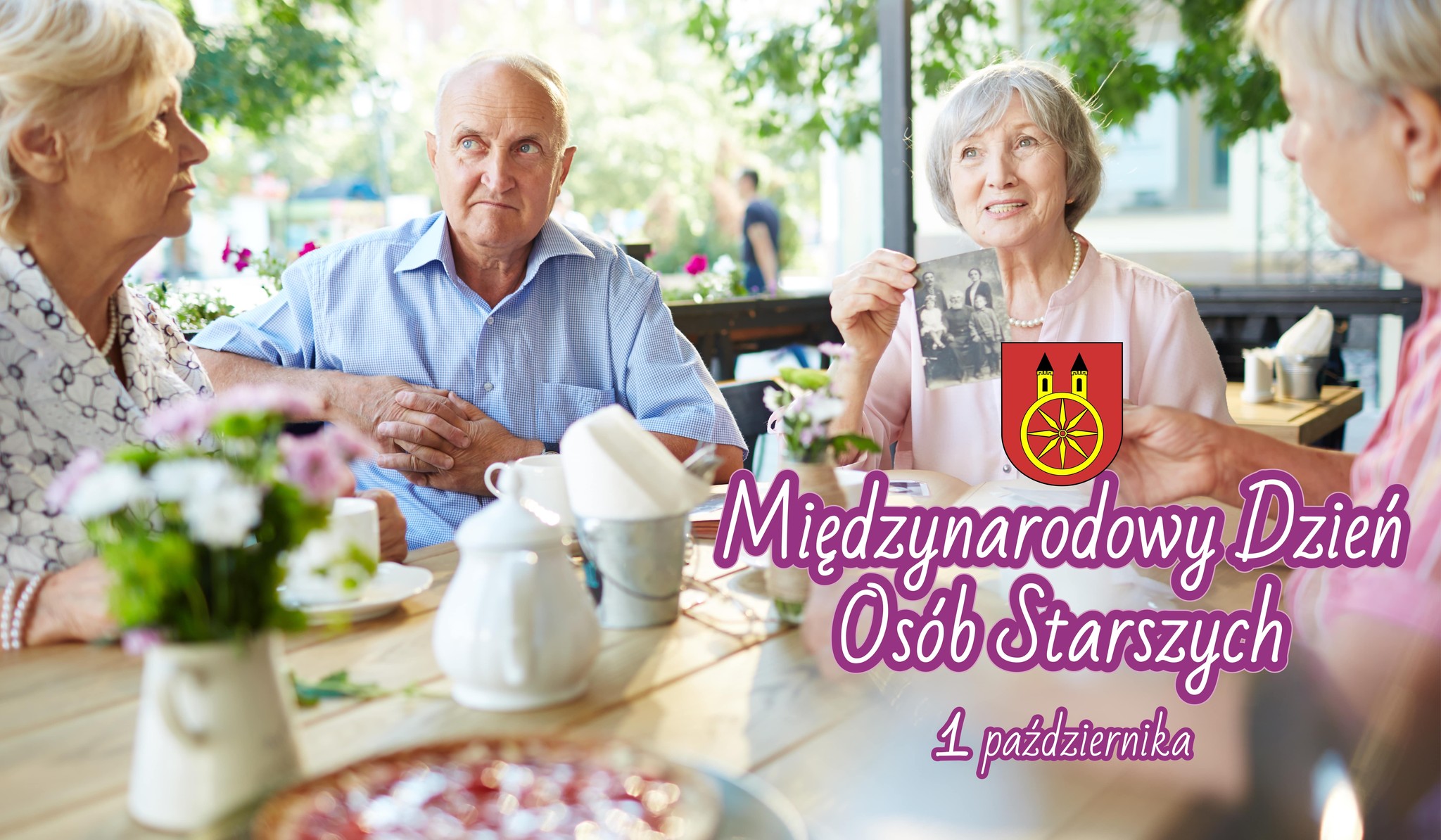 Grupa seniorów spędza wspólnie czas przy stole z okazji Międzynarodowego Dnia Osób Starszych.