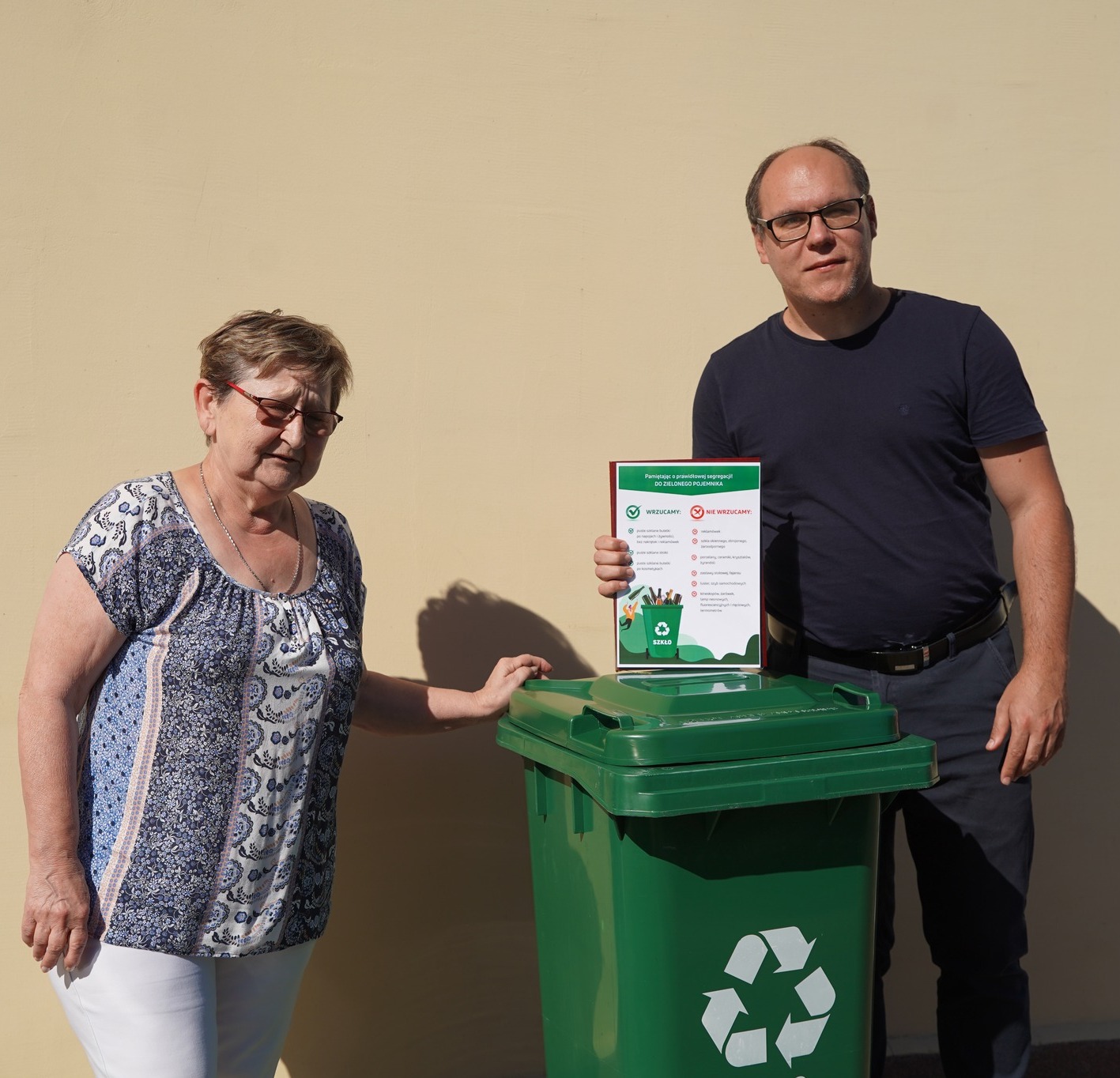 Radny Miejski Adrian Król przekazuje mieszkańce Koła zielony pojemnik do selektywnej zbiórki odpadów. W dłoniach trzyma pamiątkowy dyplom, w tle ściana budynku.