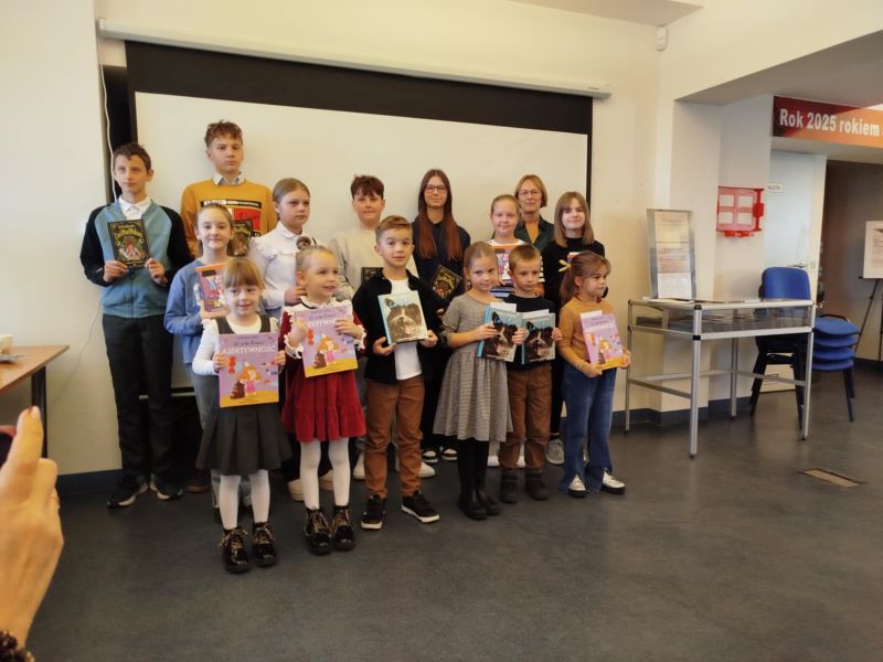 Na zdjęciu widać grupę dzieci i młodzieży stojących w kilku rzędach, trzymających w rękach książki, podczas rozdania nagród w konkursie plastycznym.