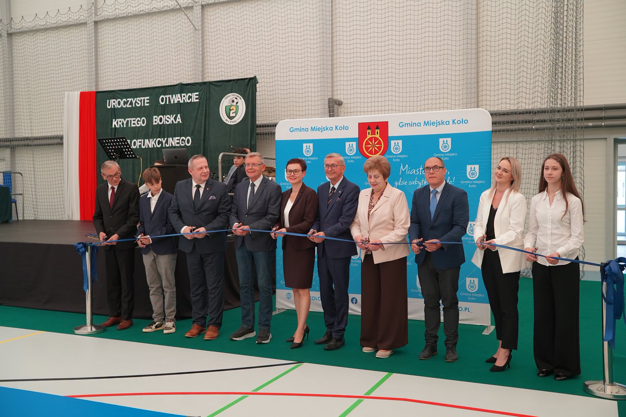 Uroczyste przecięcie wstęgi podczas otwarcia krytego boiska wielofunkcyjnego przy Szkole Podstawowej nr 2 w Kole, z udziałem władz gminy i uczniów.