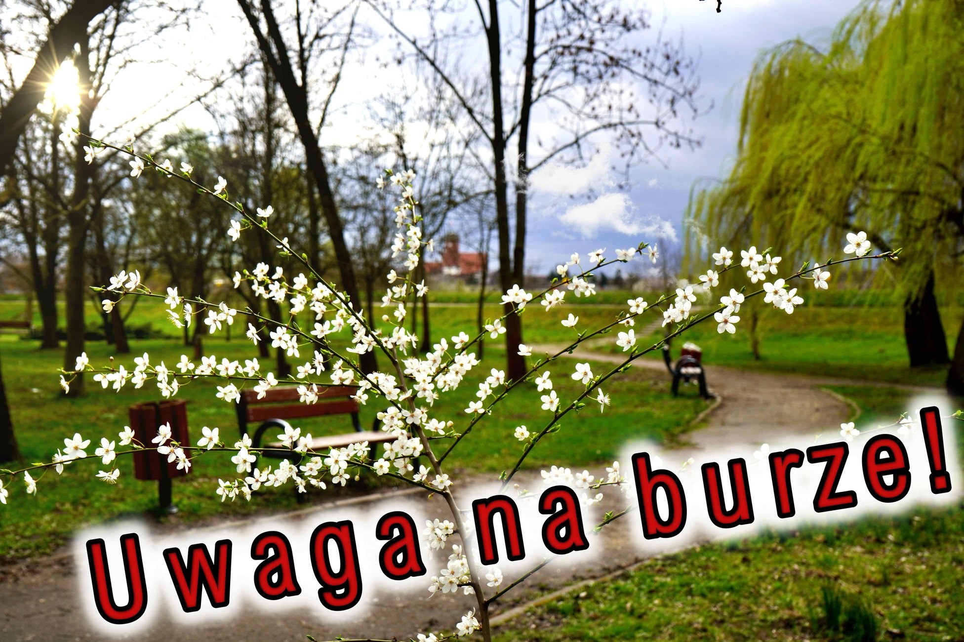 Grafika przedstawia wiosenny park z kwitnącymi gałązkami na pierwszym planie i napisem „Uwaga na burze!” w czerwonym, ostrzegawczym stylu.