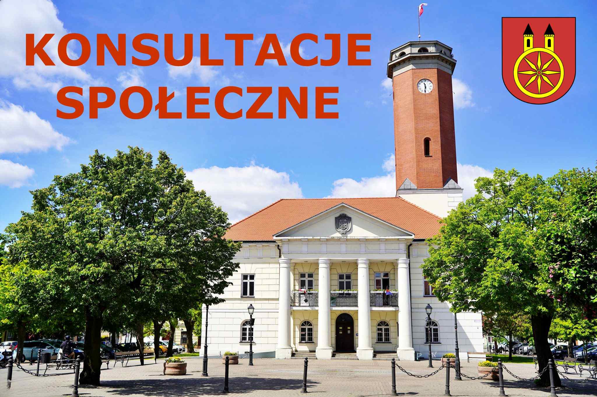 Zdjęcie przedstawia ratusz w mieście Koło. Budynek ma klasyczny wygląd, z charakterystycznymi białymi kolumnami na fasadzie, które wspierają balkon nad wejściem. Widać również czerwoną wieżę zegarowa z polską flagą na szczycie. Ratusz otaczają drzewa
