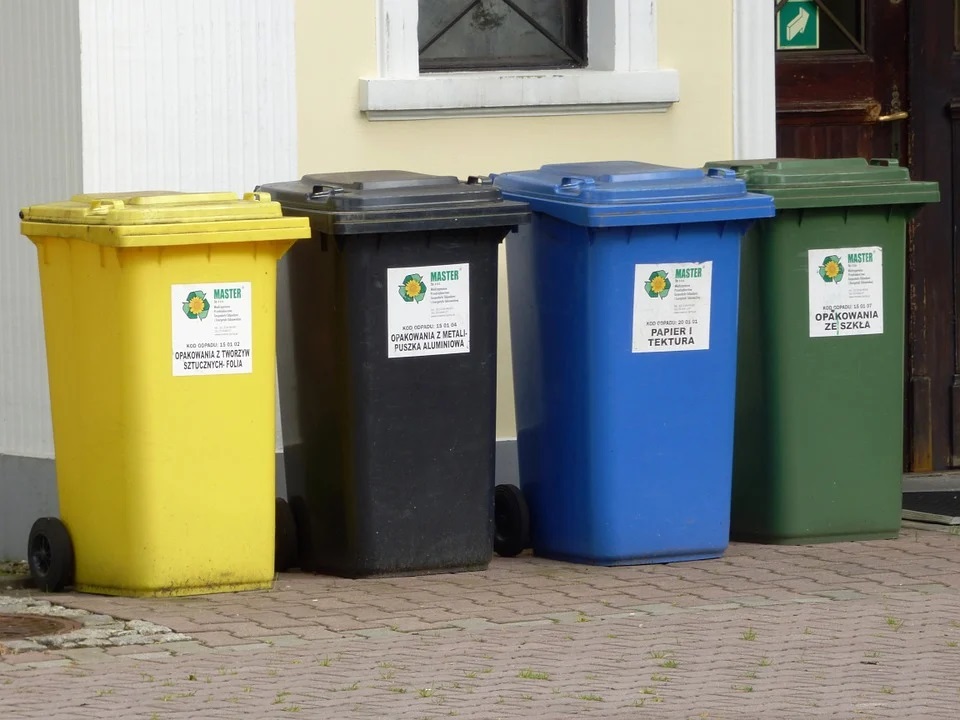 Zdjęcie przedstawia cztery pojemniki do segregowania śmieci pod domem wielorodzinnym.
