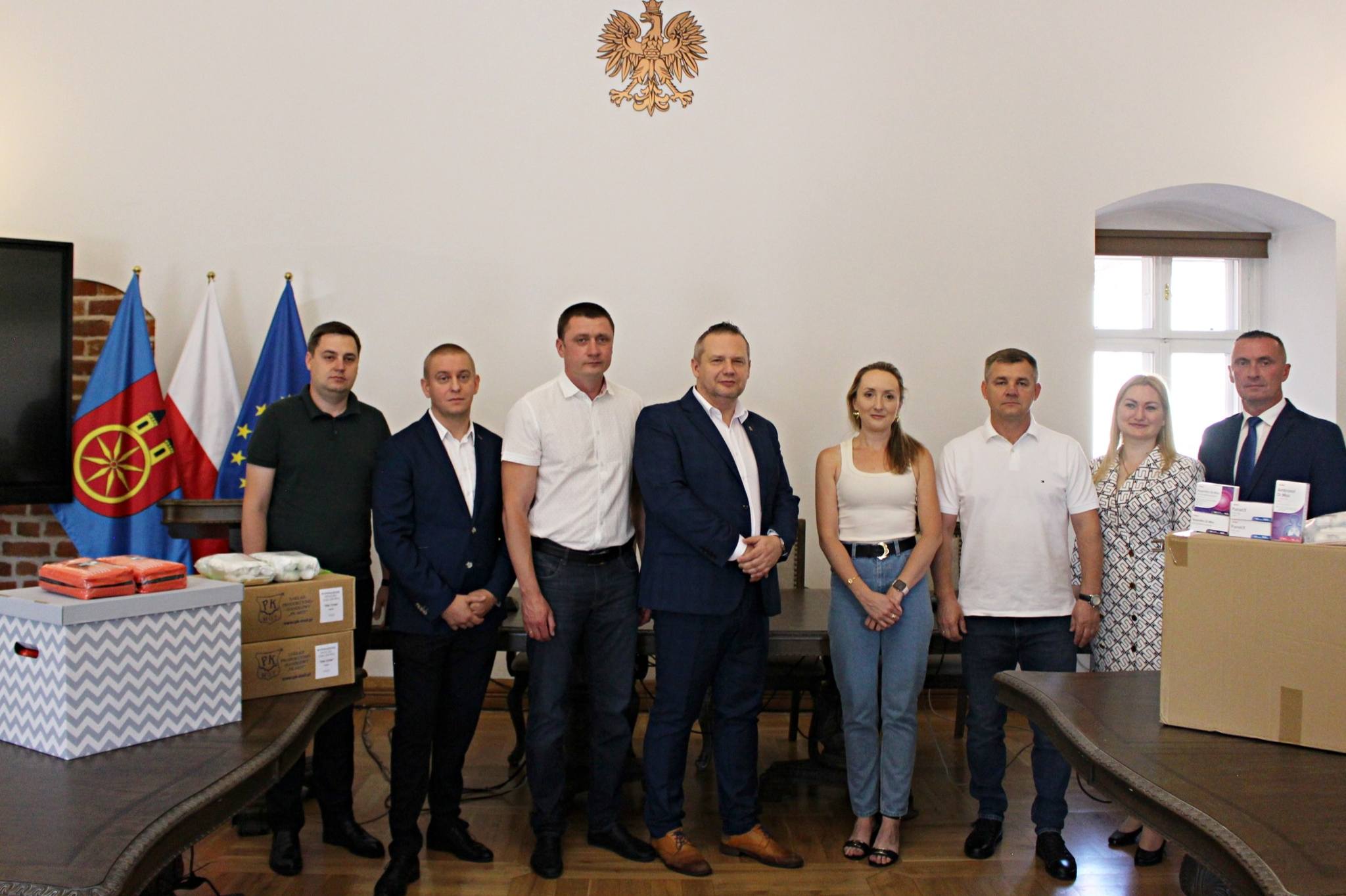 Na zdjęciu widoczna jest grupa ośmiu osób stojących w rzędzie w pomieszczeniu urzędowym