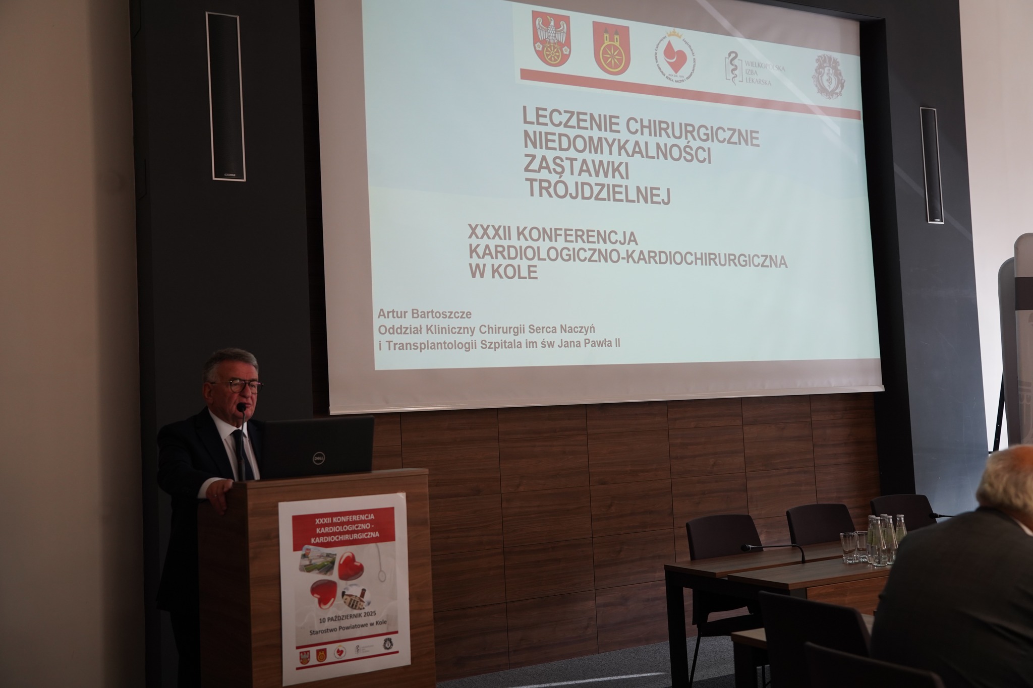 Na zdjęciu widać mężczyznę wygłaszającego prezentację podczas konferencji kardiologiczno-kardiochirurgicznej, stojącego przy mównicy z laptopem i ekranem z tytułem wykładu w tle.