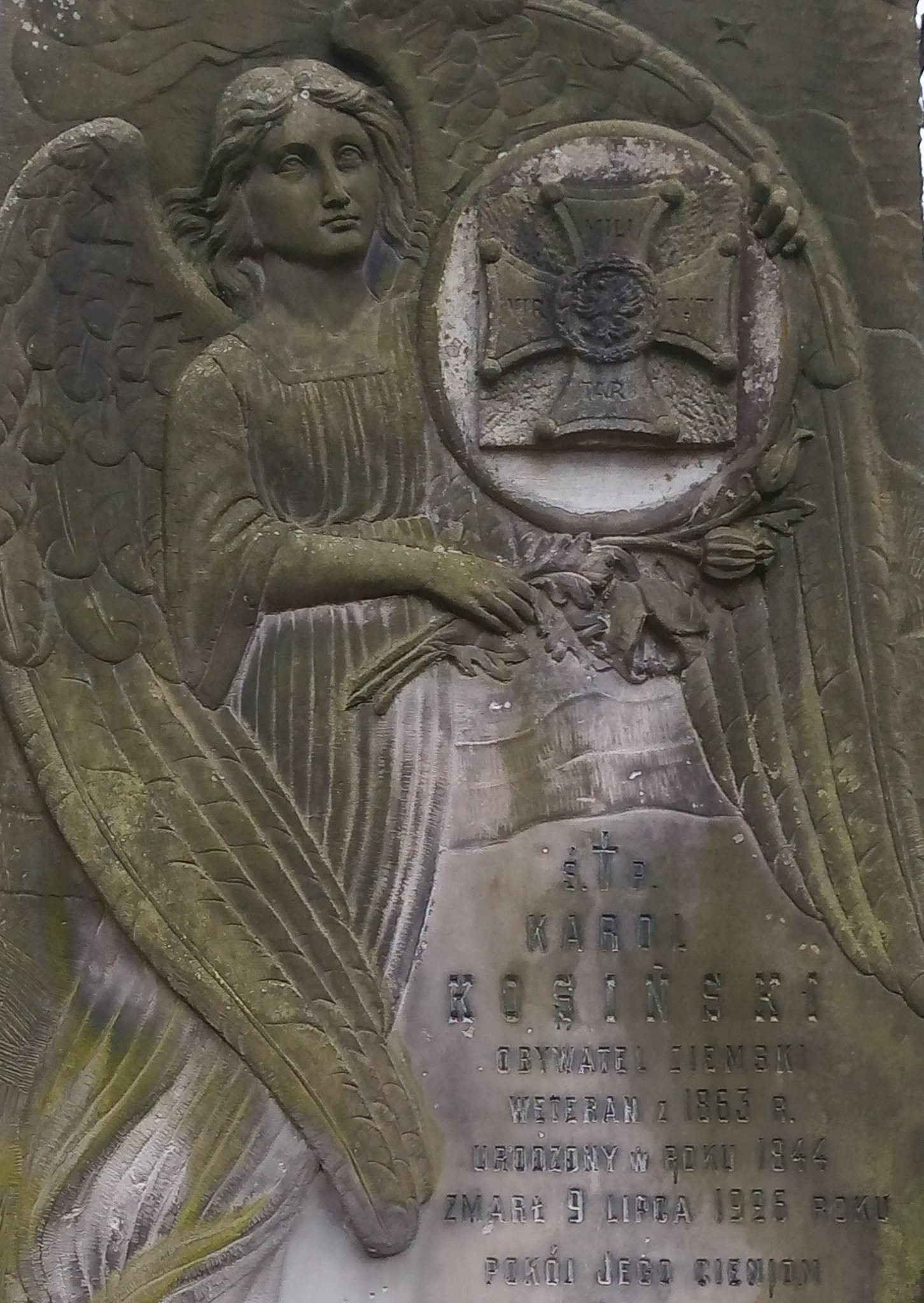 Kamienna płaskorzeźba nagrobna z postacią anioła trzymającego wieniec i medalion z krzyżem. Napis: Karol Kosiński, weteran 1863 r., ur. 1844, zm. 9 lipca 1925.