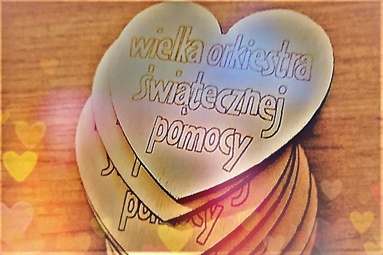 Na zdjęciu widać kilka drewnianych serduszek ułożonych na stole, z wypalonym napisem „Wielka Orkiestra Świątecznej Pomocy”. Serduszka mają naturalny kolor drewna i wyglądają jak ręcznie wykonane.