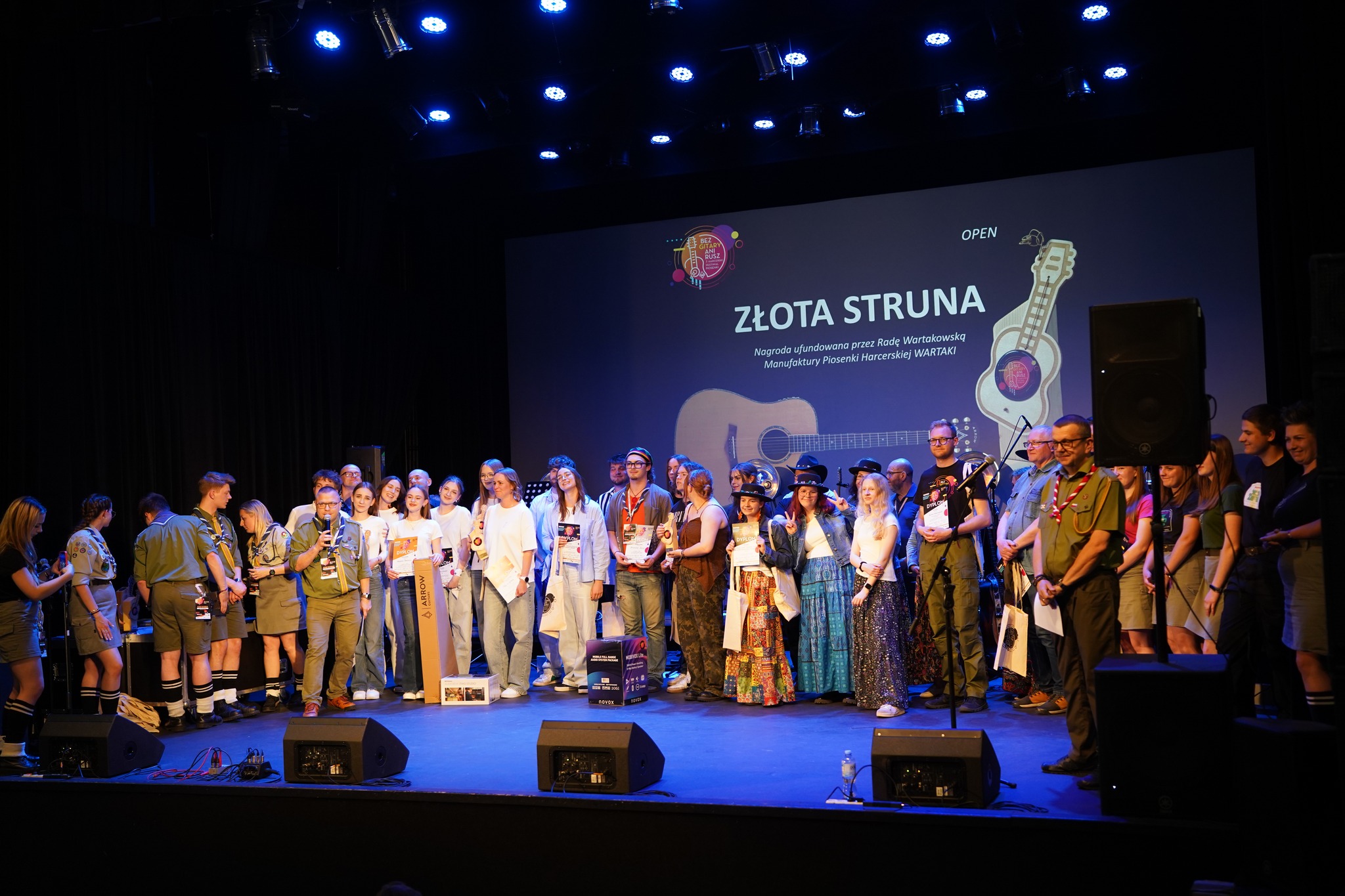 Grupa uczestników i laureatów festiwalu na scenie podczas wręczenia nagrody Złota Struna, ufundowanej przez Radę Wartakowską Manufaktury Piosenki Harcerskiej WARTAKI. Kategoria OPEN.