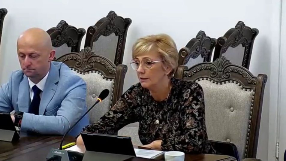 Zdjęcie przedstawia kobietę i mężczyznę siedzącego przy stole podczas obrad sesji Rady Miejskiej Koła. Kobieta jest w okularach, mówi do mikrofonu, a mężczyzna obok niej, w jasnoniebieskiej marynarce, słucha. Przed nimi znajdują się tablety.