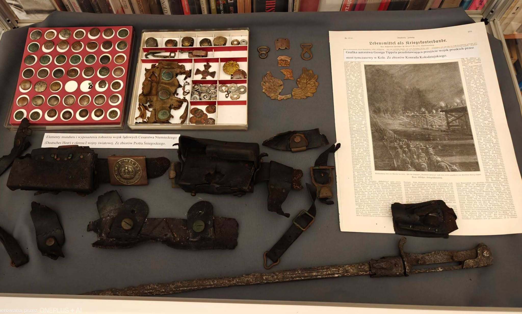 Gablota wystawowa z pamiątkami z lat 1914-1918: guziki, klamra z koroną, skórzane ładownice, bagnet oraz rycina przedstawiająca przemarsz wojsk przez most tymczasowy w Kole.