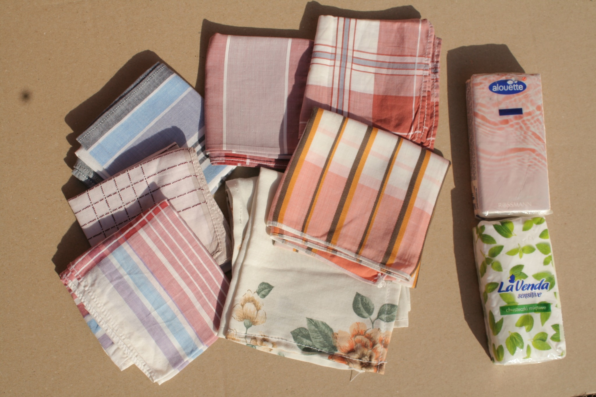 Zdjęcie przedstawia kilka materiałowych chusteczek oraz dwa opakowania papierowych chusteczek higienicznych.