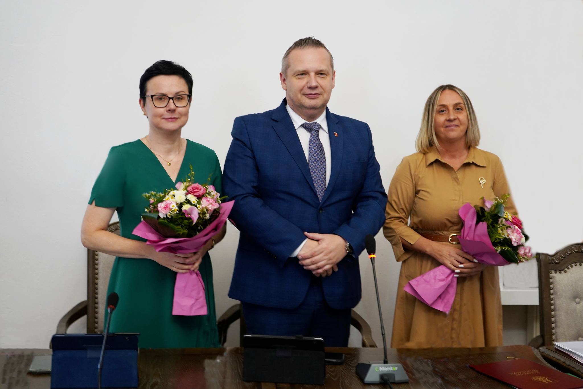 Na zdjęciu widzimy trzy osoby stojące obok siebie, dwie kobiety, a między nimi mężczyzna