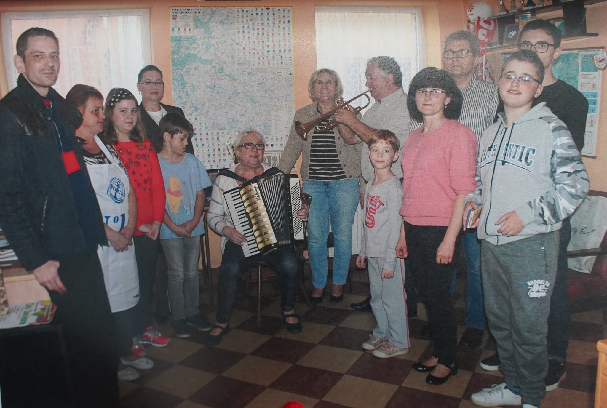 Grupa osób pozuje wspólnie przy stole podczas spotkania towarzyskiego. jeden z mężczyzn gra na trąbce, kobieta siedząca na krześle gra na akordeonie.