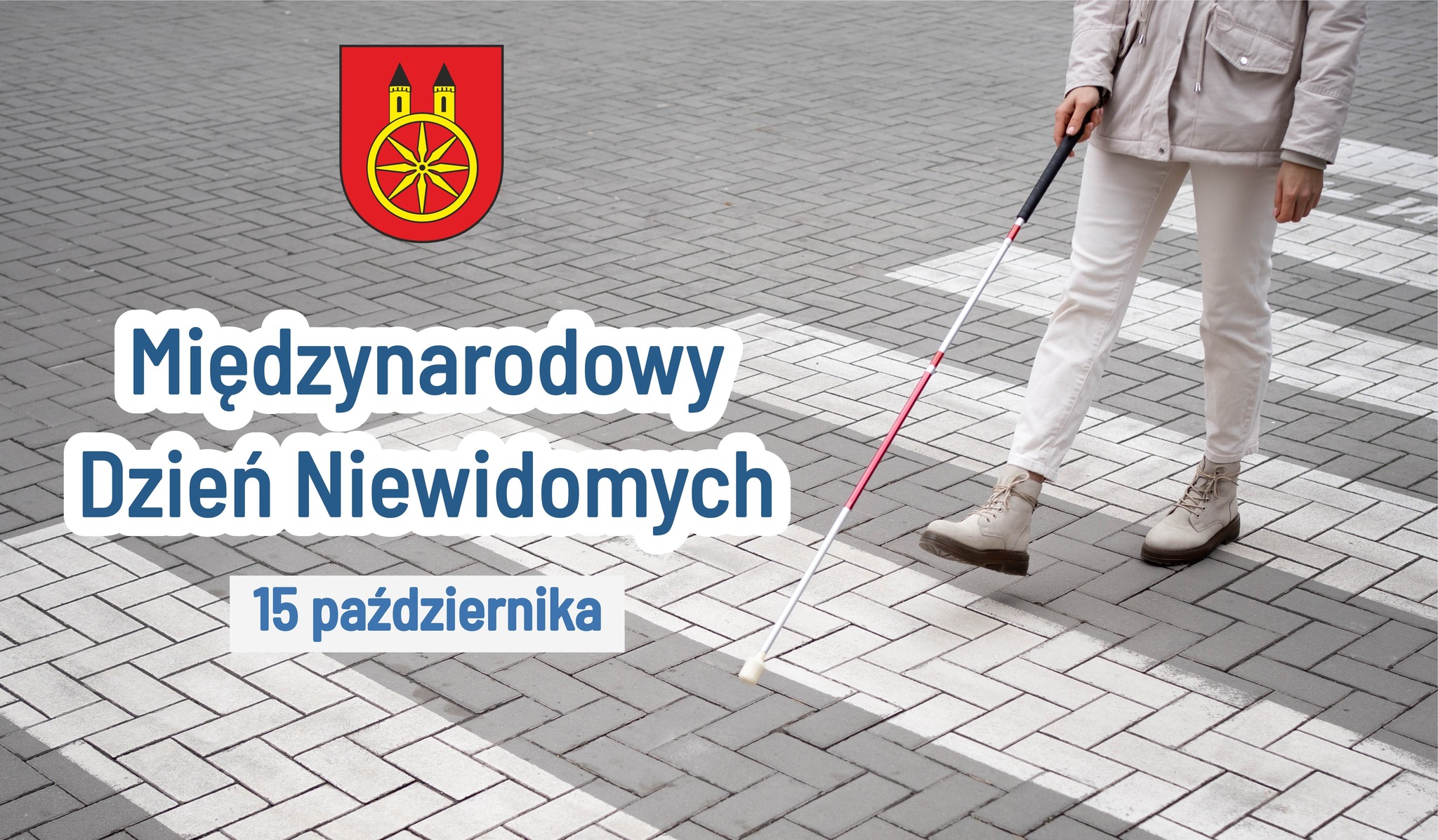 Plansza promująca Międzynarodowy Dzień Niewidomych. Z prawej strony widać kobietę z białą laską przechodzącą przez pasy . Z lewej strony napis: Międzynarodowy Dzień Niewidomych. Nad nim herb miasta Koła.