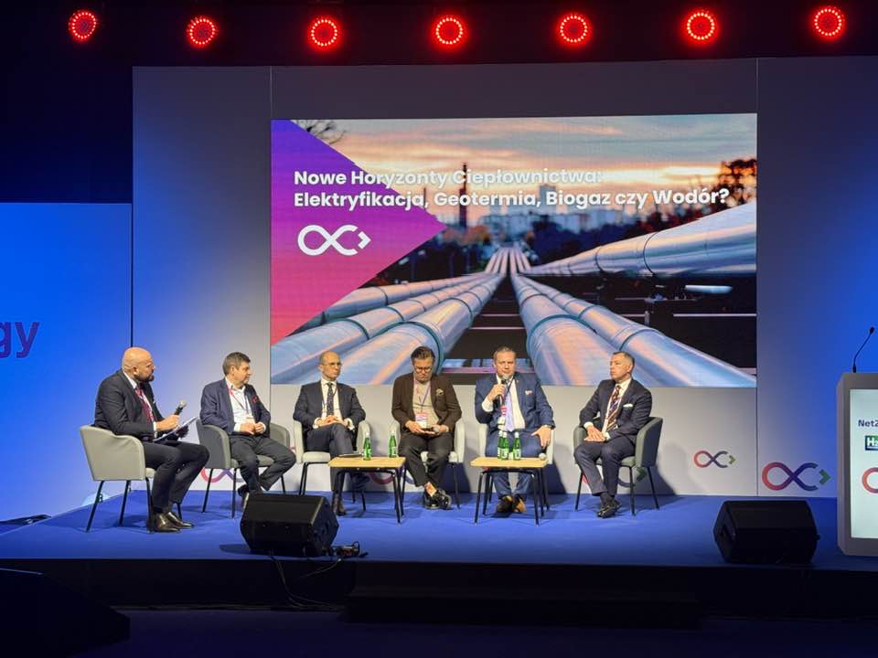 Zdjęcie przedstawia panel dyskusyjny podczas konferencji energetycznej. Sześciu mężczyzn w garniturach siedzi na scenie, a za nimi widoczny jest ekran z tematem debaty: Nowe Horyzonty Ciepłownictwa: Elektryfikacja, Geotermia, Biogaz czy Wodór?.