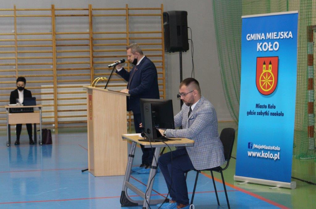 Zdjęcie przedstawia Burmistrza Miasta Koła na mównicy i siedzącego Przewodniczącego Rady Miejskiej.