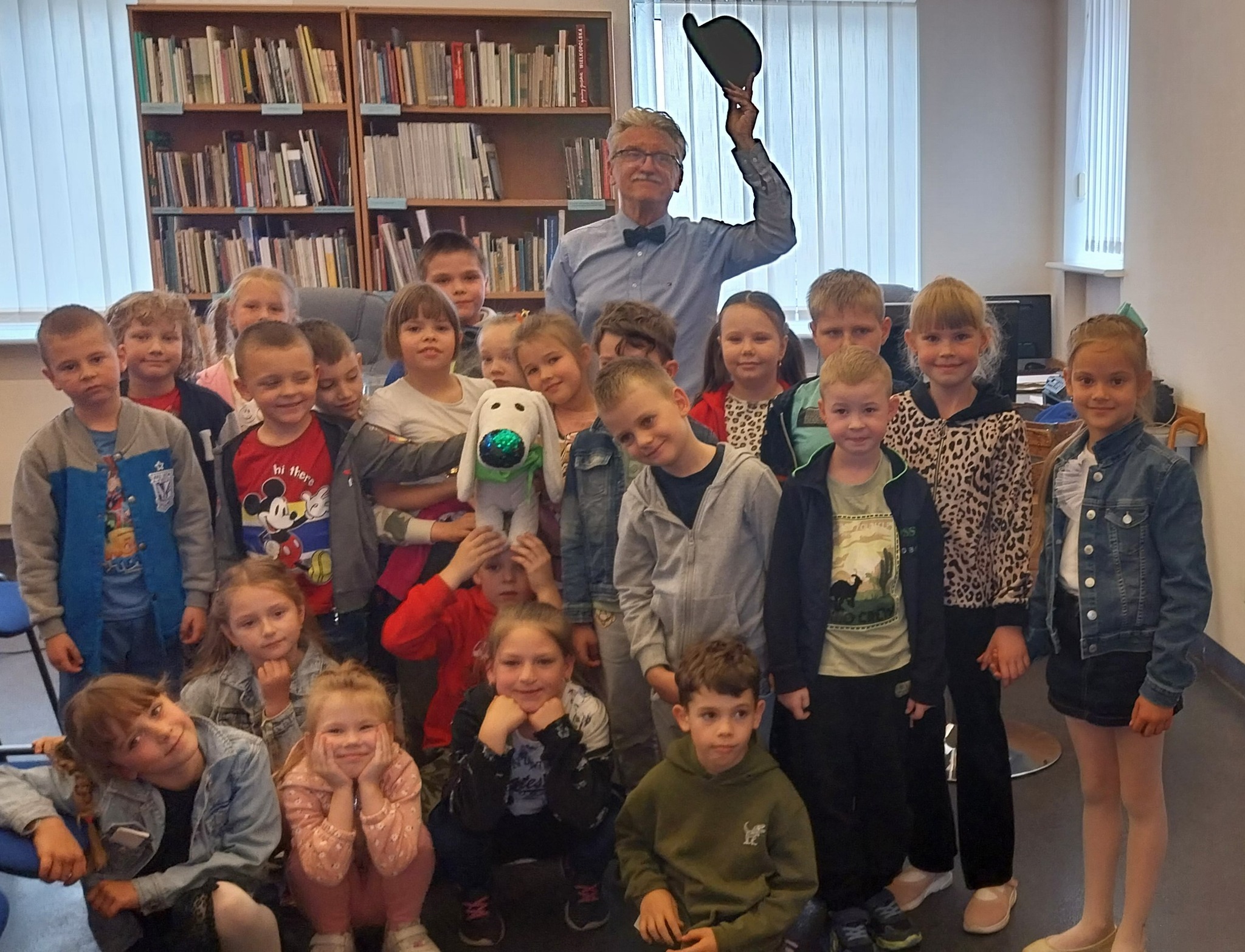 Mężczyzna z podniesionym w dłoniach czarnym kapeluszem, przed nim gromada uśmiechniętych dzieci