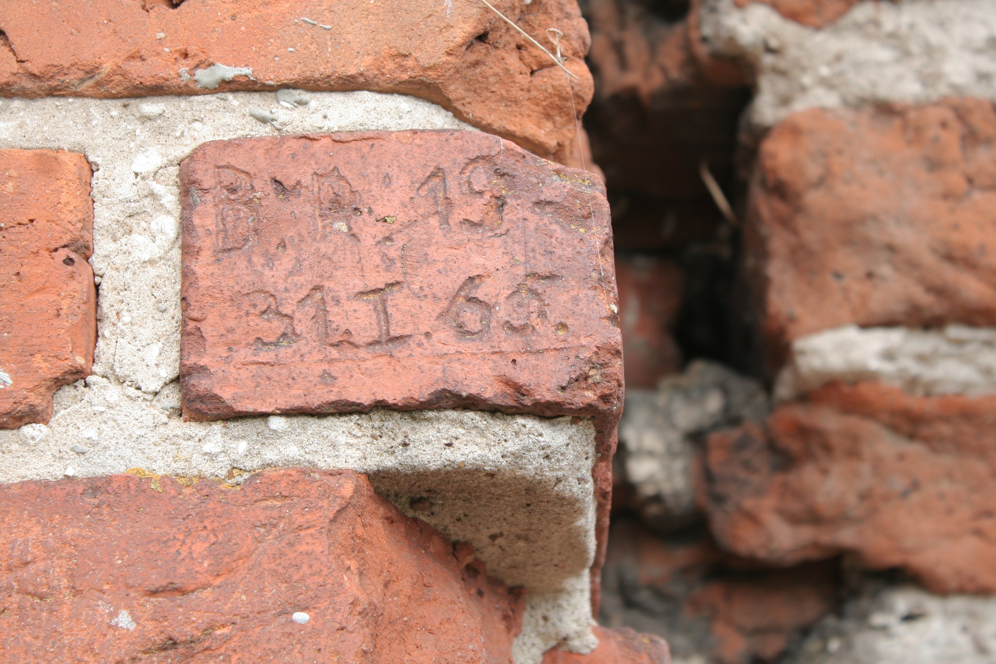 Czerwone cegły stanowiące fragment murów ruin zamku, na których widoczne są wyryte napisy i daty, będące śladem dawnych odwiedzających oraz świadectwem historii tego miejsca.