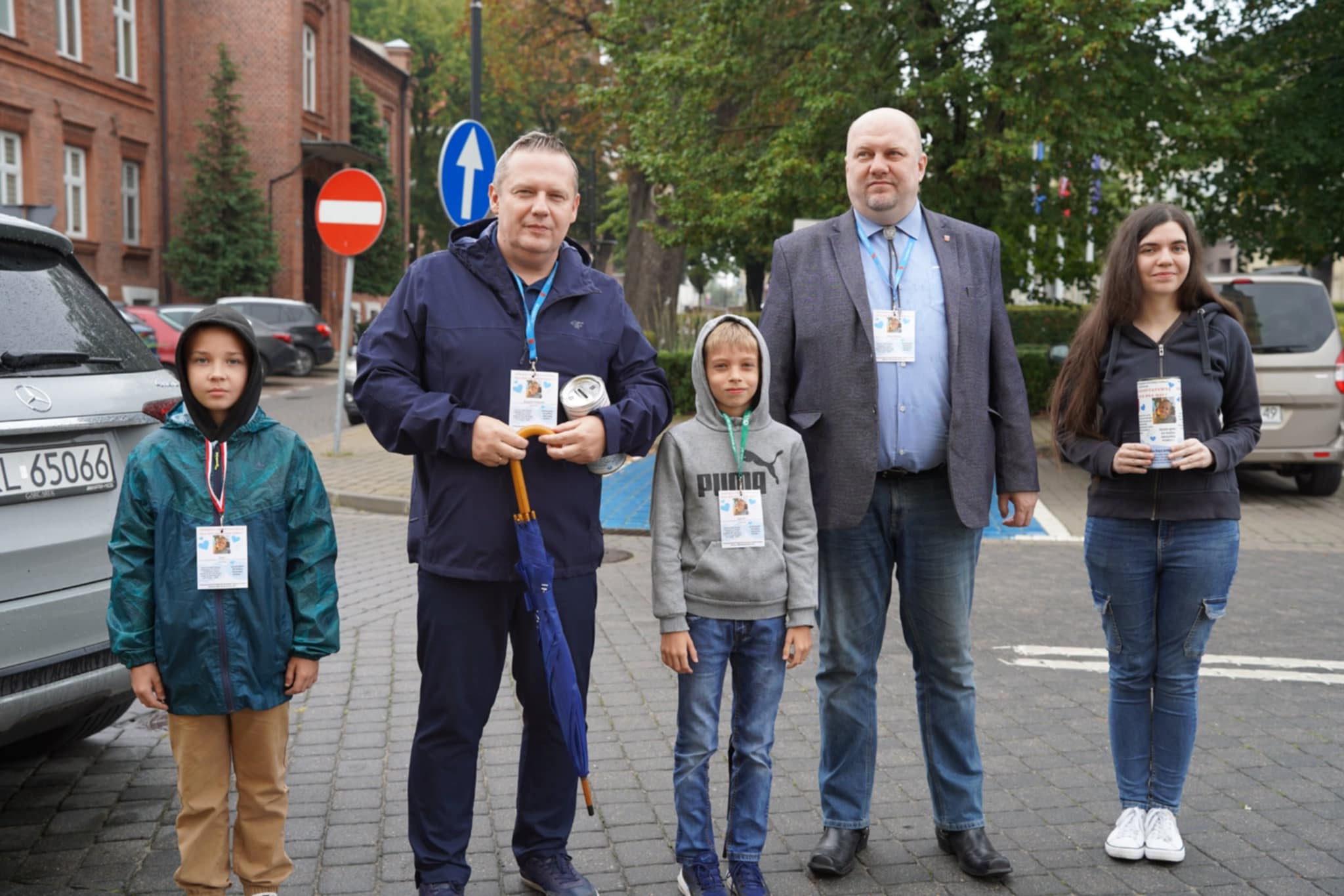 Na zdjęciu widać grupę pięciu osób stojących na ulicy, biorących udział w akcji charytatywnej – mają identyfikatory i puszki do zbiórki. W tle widać drzewa oraz budynek Urzędu Miejskiego w Kole z czerwonej cegły.